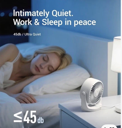 A small white desk fan sits on a bedside table next to a lit lamp in a bedroom, with a sleeping woman in bed in the background. Text on the image reads 'Intimately Quiet.