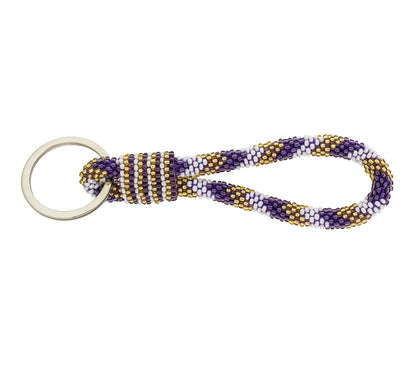 A beaded keychain with a silver metal key ring, featuring a loop of purple, white, and gold seed beads with a wrapped knot detail, shown on a plain white background.