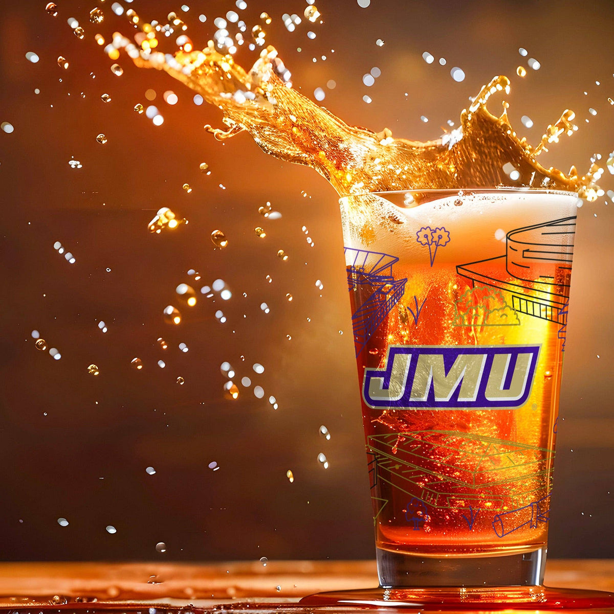 A clear drinking glass with a bold blue and purple 'JMU' logo and architectural line drawings, filled with an orange-brown beverage and captured mid-splash against a warm glowing background.