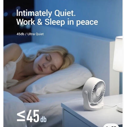 A small white desk fan sits on a bedside table next to a lit lamp in a bedroom, with a sleeping woman in bed in the background. Text on the image reads 'Intimately Quiet.
